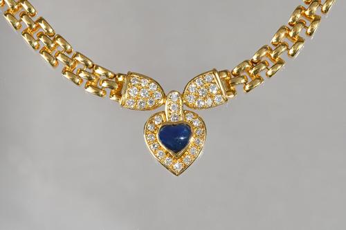 A gold, sapphire and diamond pendant necklace, the front mounted with a heart shaped cabochon sapphire, in a surround of circular cut diamonds, betwee
