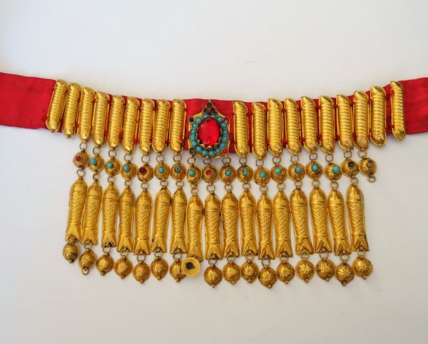 A Middle Eastern gold cased fringe necklace, the drops formed as a row of fish, otherwise mounted with pale blue and red pastes, fitted to a magenta r