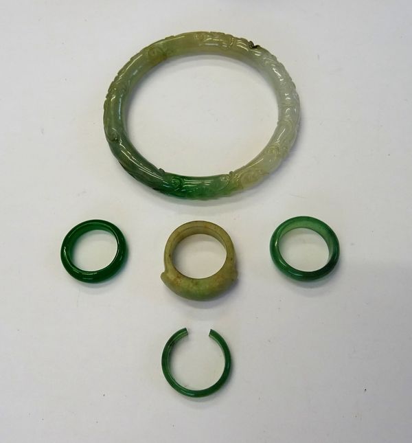 A carved jade circular bangle, with floral and scrolling decoration, a jade ring, of saddle form, a pale green stone band ring, a pale green stone ban