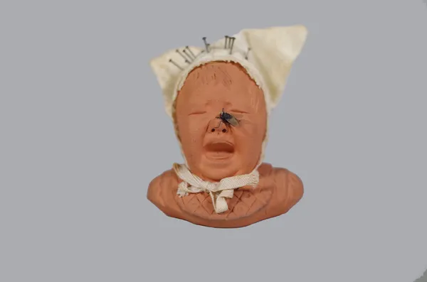 GD Paris; a novelty terracotta pincushion in the form of a crying child, white linen cap, stamped to underside, 8.5cm high.