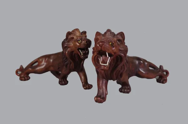 A pair of Asian carved hardwood animalier figures of prowling lions, glass inset eyes, 25cm long, (2).