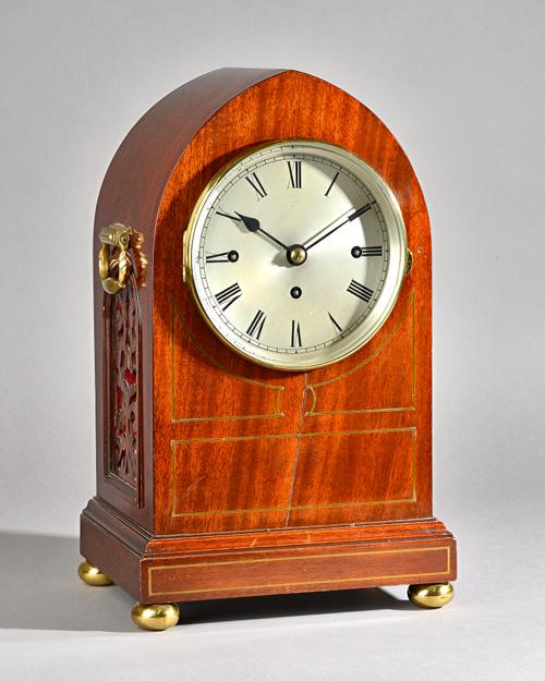 An Edwardian mahogany and brass inlaid bracket clock of lancet form, with silvered dial and twin brass handles over pierced fret work sides, a plinth