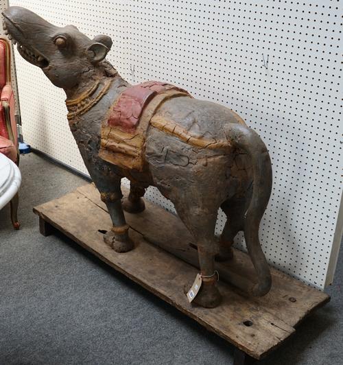 A polychrome painted Indian carved wooden figure depicting Vahana in the form of Mooshak, symbol of good luck, on a wooden plank base, 142cm wide.