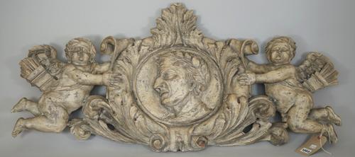 A North Italian limed pine wood wall applique, or door surmount, central carved with a bust of a Romanesque male flanked by two Cupid figures, 110cm w