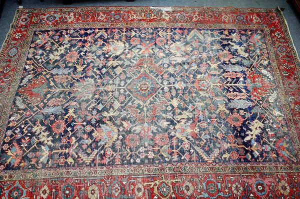 An Heriz carpet, Persian, the dark indigo field with a central madder diamond, with bold palmettes extending, angular leaves and flowers, a madder pal