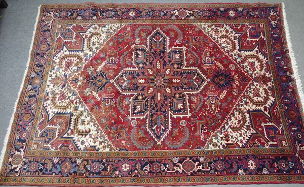 An Heriz carpet, Persian, the madder field with a bold indigo medallion, ivory spandrels, all with angular leaves, palmettes and floral sprays, an ind