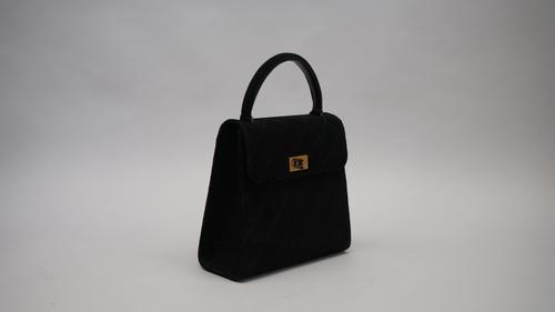 A Chanel quilted black suede evening bag with top carrying handle to a single flap fastening with gold tone hardware clasp, 22.5cm wide.