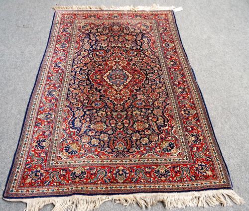 A Kashan rug, deep blue field with symmetric design of carmine lobed central medallion within similar spandrels and main border, 206cm x 130cm.