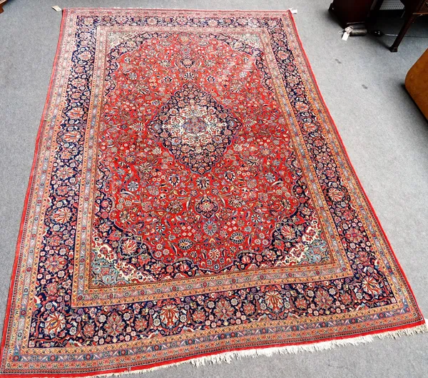 A Kashan carpet, Persian, the madder field with a bold indigo and ivory medallion, matching spandrels, all with abundantly floral sprays, a dark indig