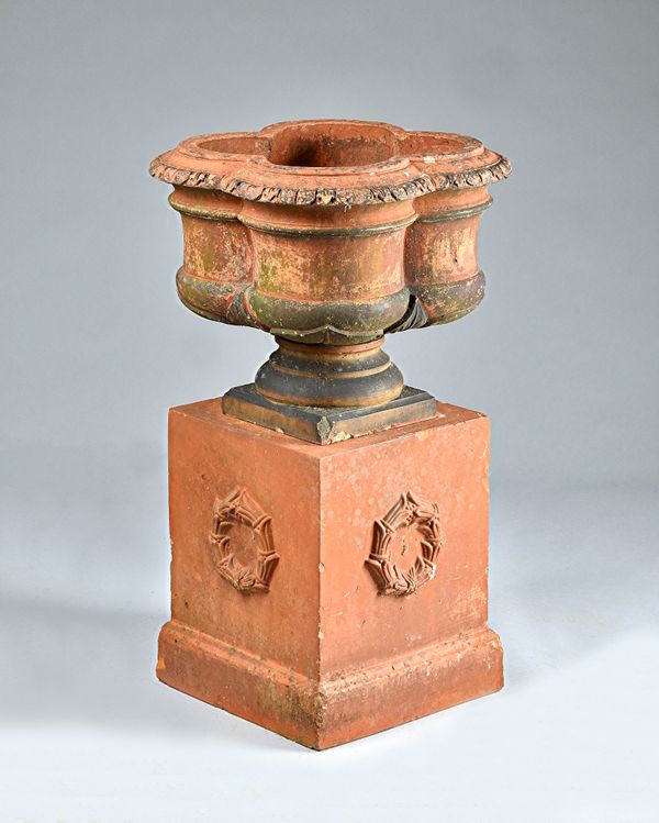 A terracotta jardiniere, the lobed quatrefoil body on turned socle and square pedestal, 53cm wide x 86cm high. Illustrated.