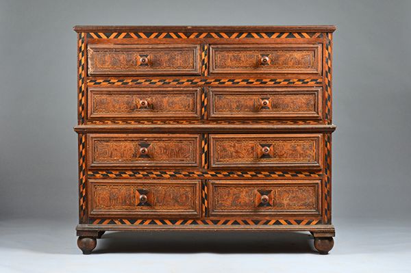 A late 17th century oak two part chest of eight short drawers, each with chequer banding and rolled paper/ marblewood veneered fronts, on bun feet, 12