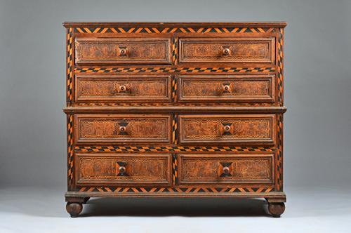 A late 17th century oak two part chest of eight short drawers, each with chequer banding and rolled paper/ marblewood veneered fronts, on bun feet, 12