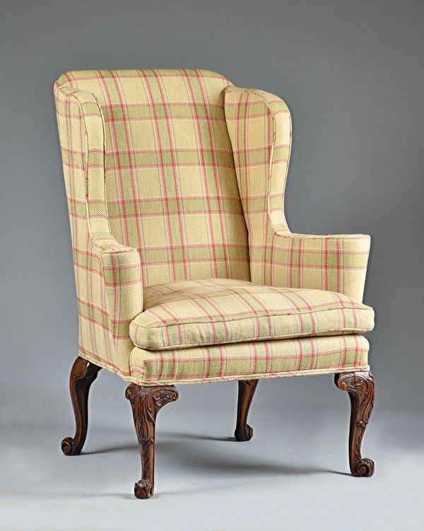 A George II style wingback armchair, on carved scrolling walnut supports, 85cm wide x 116cm high. Illustrated.