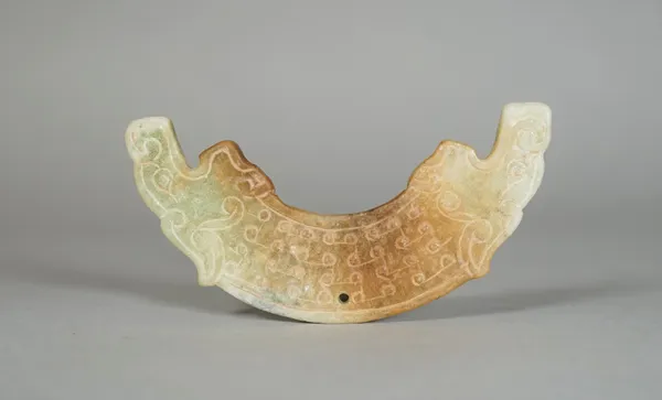 A Chinese archaistic jade huang, carved with dragon head ends, the stone of pale celadon and russet tones, 9.5cm. wide.