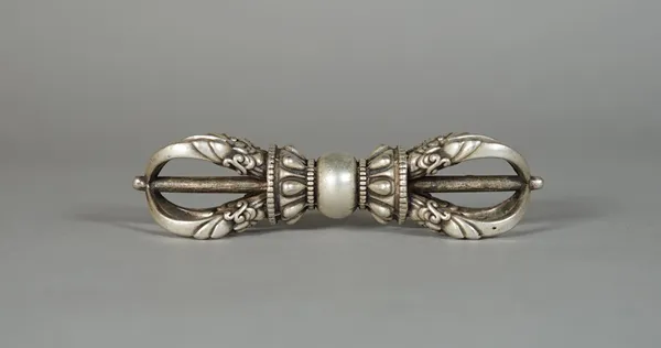 A Tibetan silver metal thunderbolt ( vajra), of traditional form, a lightning bolt at each end, 9.5cm.length.