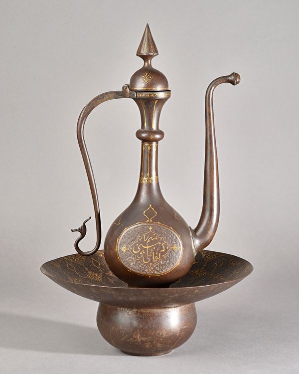 A Qajar gold-damascened ewer and basin, 19th century, the ewer on spreading foot, the bulbous body damascened each side with script, beneath a slender