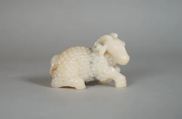 A Chinese jade figure of a ram, 19th/20th century, carved in recumbent pose, the stone of cream tone with grey and russet inclusions, 6cm.length.