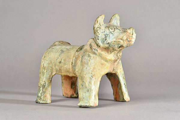 A Chinese green-glazed pottery figure of a dog, probably Han dynasty, standing four square with curly tail and wearing a combination bridle-collar, 22