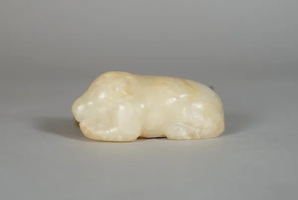 A Chinese jade figure of a recumbent dog, possibly 17th century, the stone of cream tone with russet inclusion, 5.5cm. length.