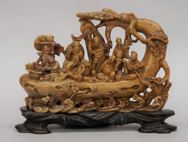 A Chinese soapstone carving, late 19th/20th century, carved with the eight Immortals on a tree trunk raft, 18.5cm. wide, wood stand, (2).