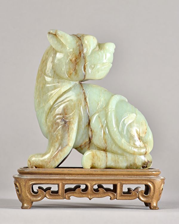 A large Chinese celadon jade figure of a mythical beast,17th century or later,  carved seated with head turned across its back, the stone with russet