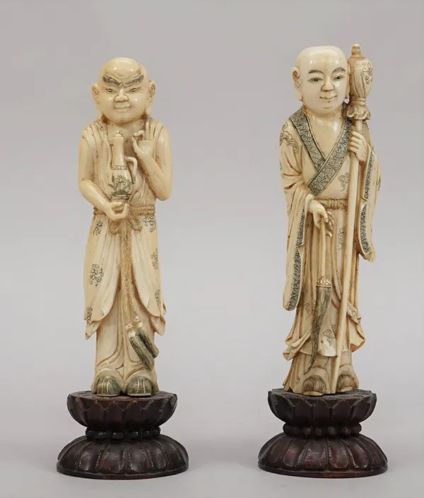 A pair of  ivory figures of luohans late 19th/early 20th century, each standing, one holding a coffee pot, the other with a fly whisk and staff, 15cm.