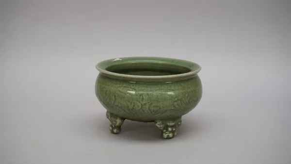 A Chinese celadon tripod censer, Ming dynasty, the compressed circular body incised with flowers and leaves, raised on three mask supports, 19.5cm. di