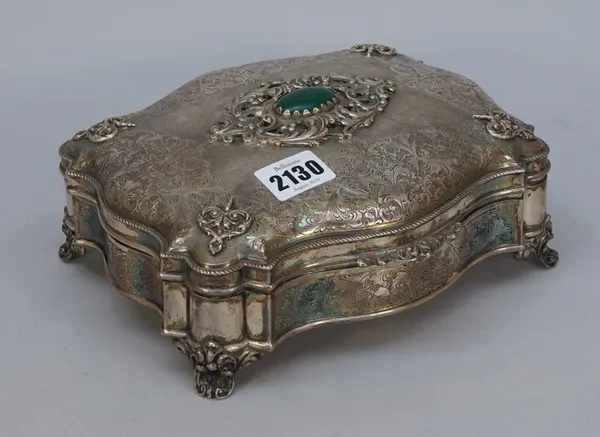 A shaped rectangular hinge lidded trinket box, the hinged lid with a cabochon green gem set centre, within a scrolling surround, the four corners with