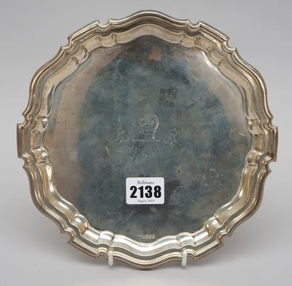 A silver salver of shaped circular form, crest and motto engraved, within a pie-crust rim in the Chippendale style, raised on three feet, the undersid