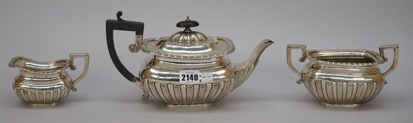 A late Victorian silver three piece tea set, comprising; a teapot, having black fittings, a twin handled sugar bowl and a milk jug, each piece with pa