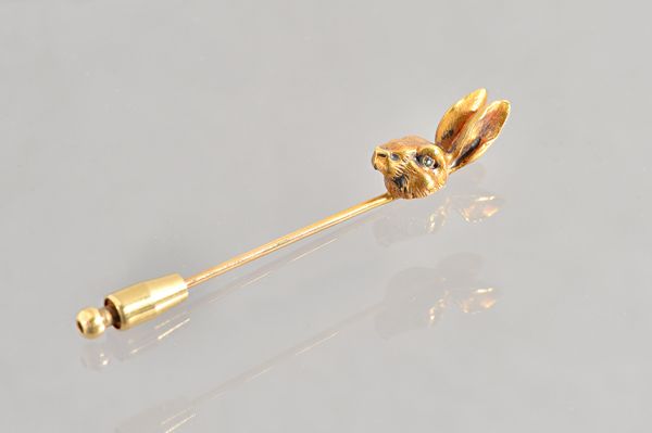 A gold stick pin, the finial modelled as a hare's head, with green gem set eyes, gross weight 7.8 gms. Illustrated.