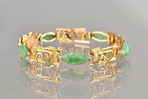 A gold and jade bracelet, the links in a rectangular openwork abstract design, with a textured finish, mounted with five marquise shaped jades at inte