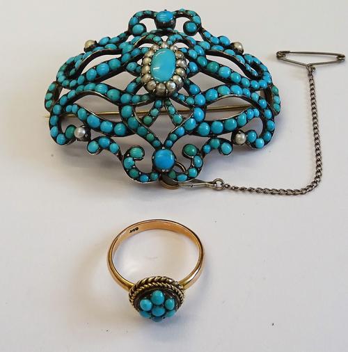 A turquoise and seed pearl set brooch, in a shaped oval scroll pierced design, mounted with the principal oval turquoise to the centre, in a surround