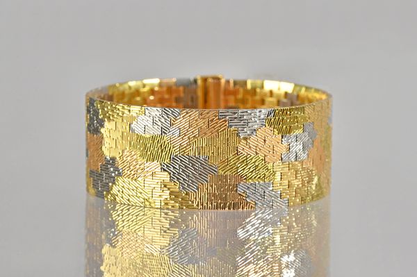 An 18ct three colour gold bracelet, in a wide abstract design, having a textured finish, on a sliding clasp, London 1965, weight 74 gms. Illustrated.