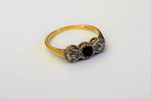 An 18ct gold, sapphire and diamond set three stone ring, mounted with a cushion shaped sapphire to the centre, between two cushion shaped diamonds, ri