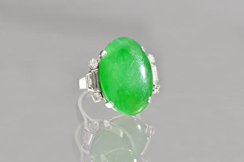 A jade and diamond ring, claw set with the oval jade to the centre, between diamond set shoulders, each shoulder mounted with two circular cut diamond