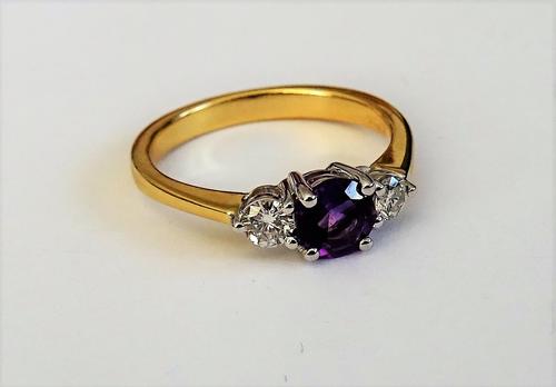 An 18ct gold, amethyst and diamond set three stone ring, claw set with the circular cut amethyst to the centre, between two smaller circular cut diamo