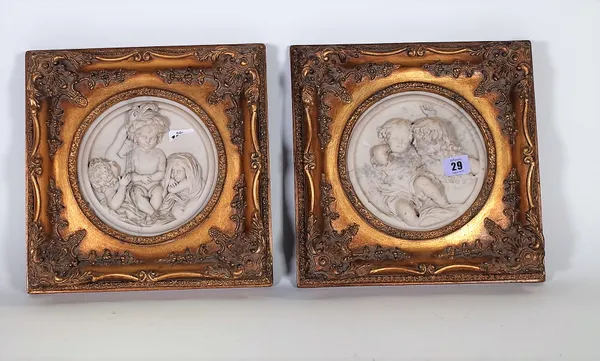 A pair of modern reconstituted circular marble plaques, each relief carved with cherubic figures in a giltwood square frame, plaques 17cm diameter, (2