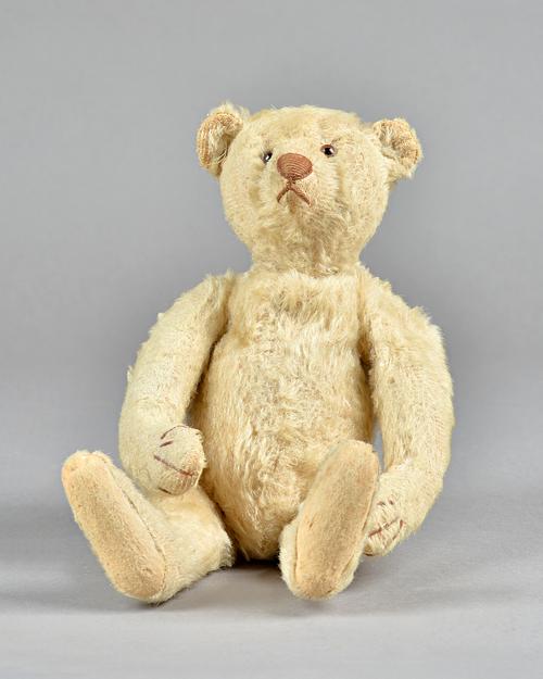 An early 20th century Steiff style teddy bear with plush golden fur, glass eyes, stitched snout, hump back and jointed limbs, 30cm high.