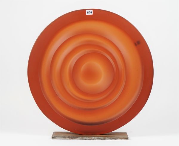 A large orange glass centre piece, of circular concentric form, unsigned, on a steel plinth, 59cm diameter.