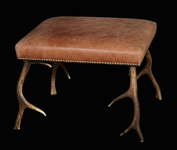 A modern rectangular footstool with brown leather upholstery on deer antler supports, 61cm wide x 45cm high.