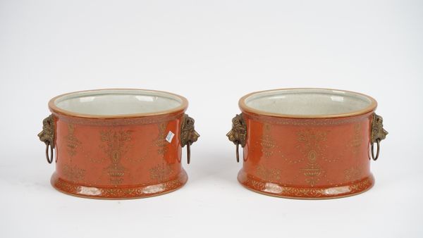 A pair of modern Thomas Goode pottery jardinières, each with twin gilt metal lion ring handles against a gilt red oval ground, 31cm wide, (2).