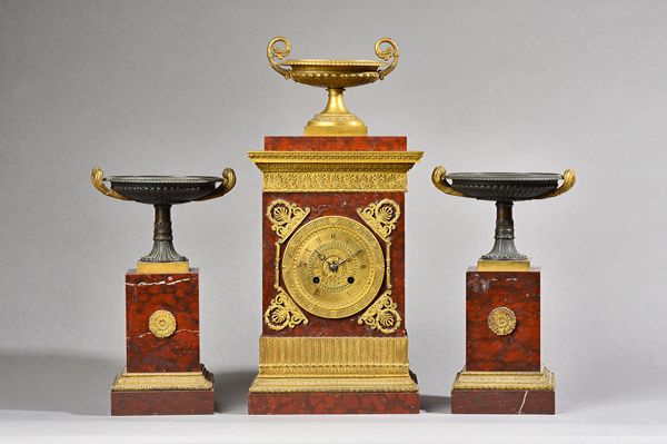 A French empire style ormolu mounted rouge marble mantel clock garniture C.1860, with urn surmount over a rectangular body enclosing a two train movem