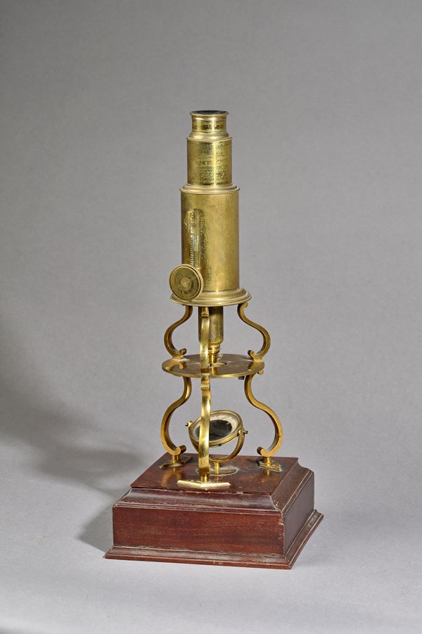 A  Continental brass monocular microscope, C.1850, with rack and pinion adjustment over triform supports and a mahogany base with frieze drawer enclos