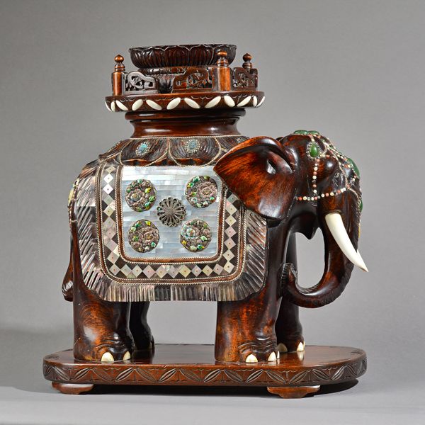 An Indian hardwood elephant circa 1900, with enamelled silver and mother of pearl decoration, inset with coloured hardstones on a foliate carved plint