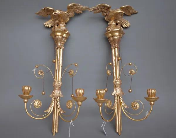 A pair of Empire style giltwood two branch wall appliques, modern, each surmounted with an eagle and hung with chains over a tri-form body, 60cm high.