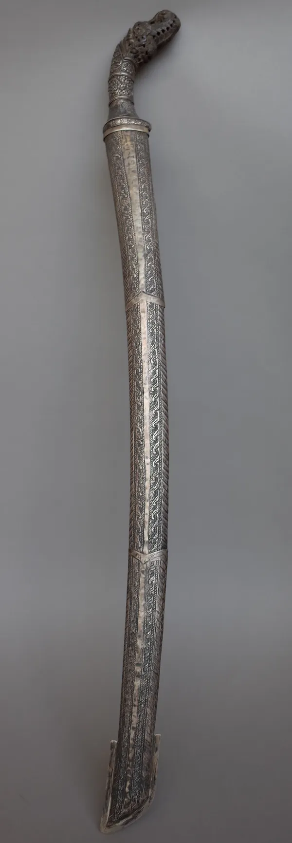 A South East Asian sword, 19th century with curved steel blade, 67cm and a foliate embossed white metal and carved wood handle in a white metal bound
