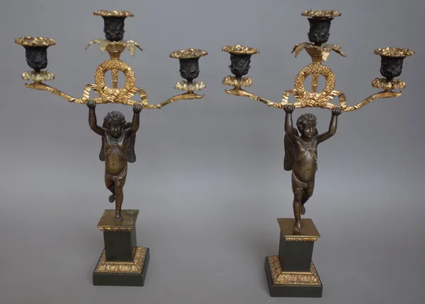 A pair of French gilt and patinated bronze Empire revival figural, three branch candelabra, each central angel on a stepped square plinth, 42.5cm high