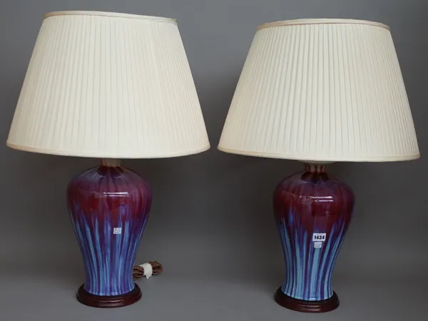 A pair of modern Chinese style flambe pottery table lamps, each of baluster form on a wooden base with cream pleated shades, 70cm high overall. (2)