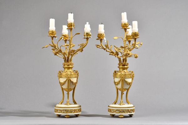 A pair of French Louis XVI style ormolu and white marble four branch candelabra, each urn issuing four foliate cast branches, with Bacchus cast masks